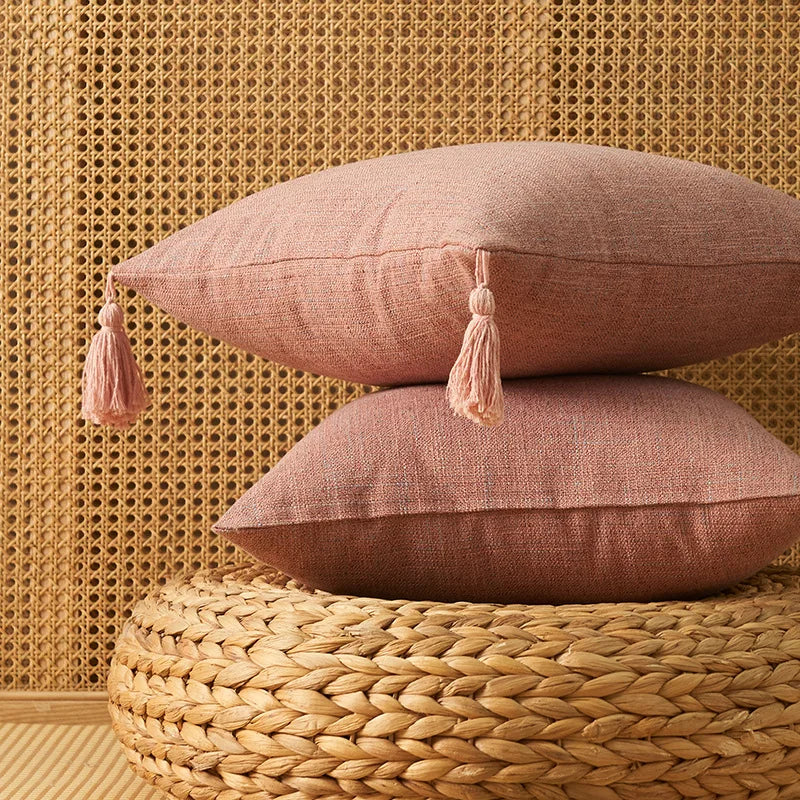 Two dusty rose linen throw pillows resting on a woven natural fiber surface against a textured gold background.