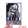 Black embroidered patch featuring a skull with hands covering its face and the text STAY POSITIVE