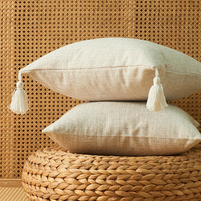 Two beige linen throw pillows resting on a woven natural fiber surface against a textured wall.