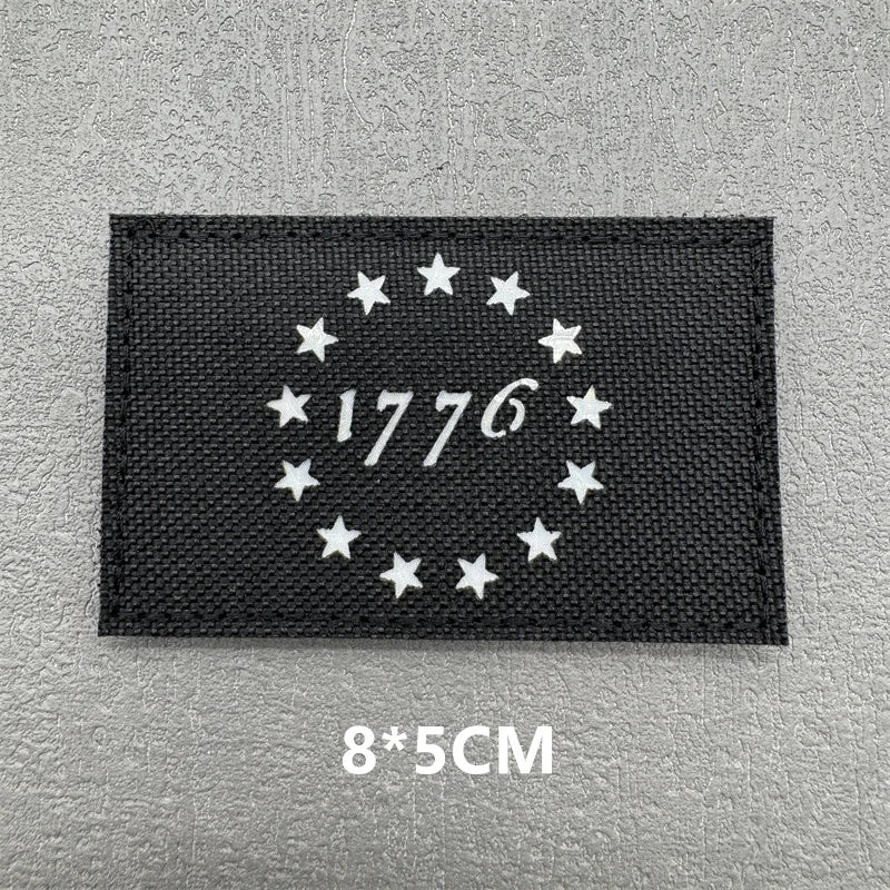 Black fabric patch with white embroidered stars and the year 1776 on a gray background