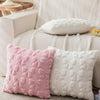 A set of two pink and white faux fur pillow covers resting on a light-colored sofa.