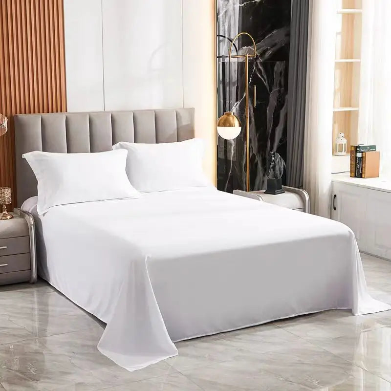 White premium flat bed sheet spread on a bed with a padded headboard and dark curtains.