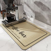 A silver insulated coffee cup drainer mat is placed on a white marble surface next to a coffee grinder.