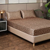 A bed with a leopard print satin sheet set featuring brown and black spots, resting on a beige frame.