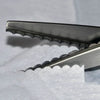A pair of professional dressmaking pinking shears with serrated blades resting on white fabric.