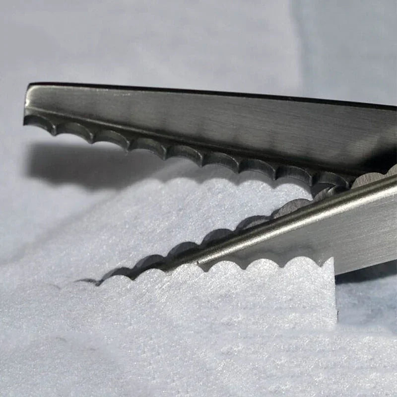 A pair of professional dressmaking pinking shears with serrated blades resting on white fabric.