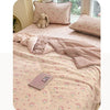 A pink cartoon quilting comforter with a floral pattern is displayed on a bed, featuring a matching pillow and blanket.