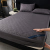 A gray quilted mattress protector is shown on a bed, featuring a diamond pattern and deep pockets.