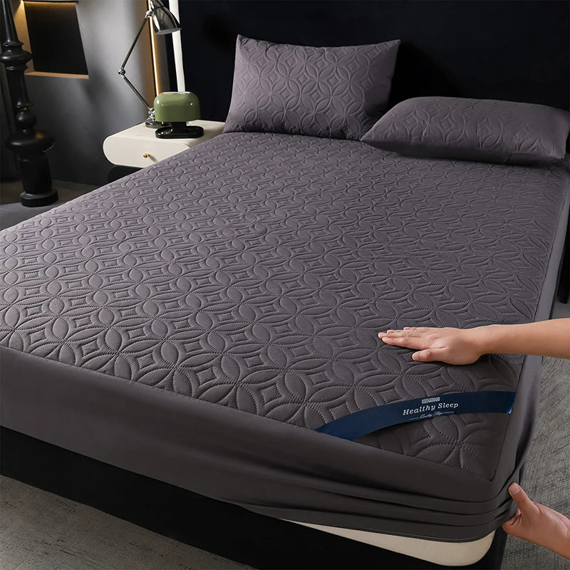 A gray quilted mattress protector is shown on a bed, featuring a diamond pattern and deep pockets.