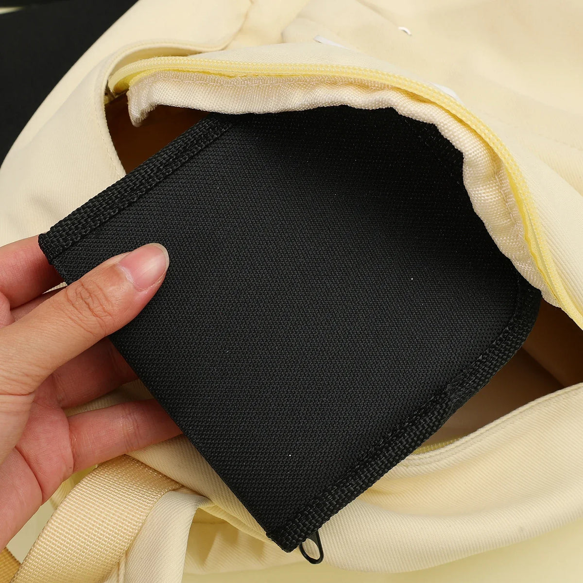 A hand is holding a black fabric pouch inside a light beige or cream colored fabric bag.