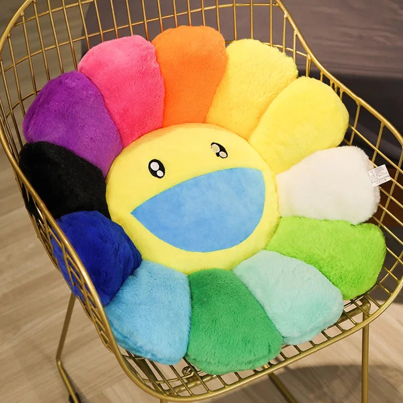 A round, yellow sunflower plush cushion with a smiling face surrounded by colorful, fluffy fabric petals in a gold wire baske