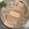 A tan foldable tote bag laid flat on a wooden surface with green foliage nearby.