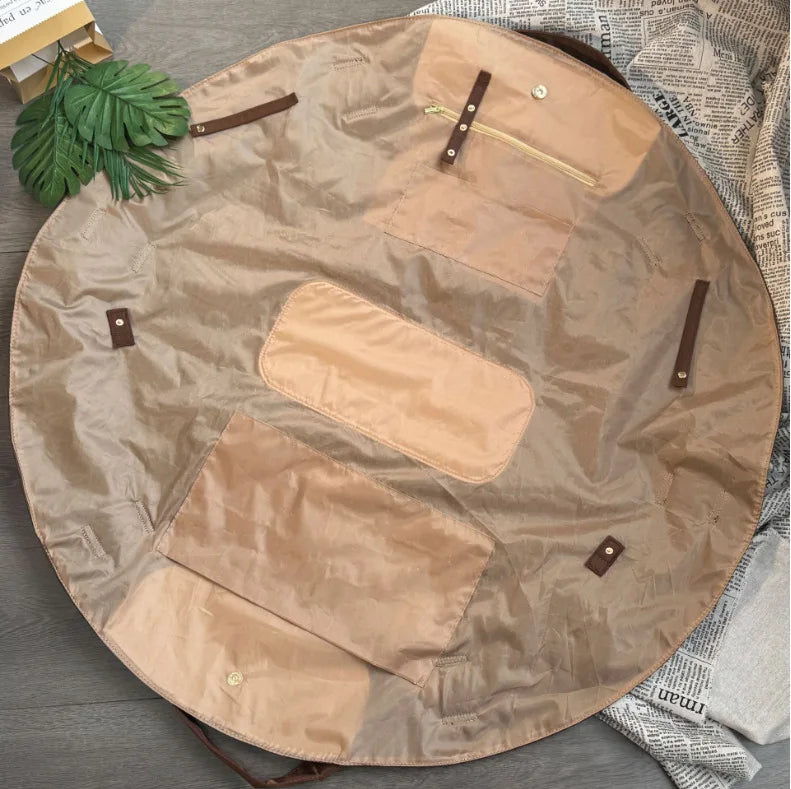 A tan foldable tote bag laid flat on a wooden surface with green foliage nearby.