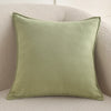 A square, olive green chenille throw pillow cover resting on a light beige sofa.
