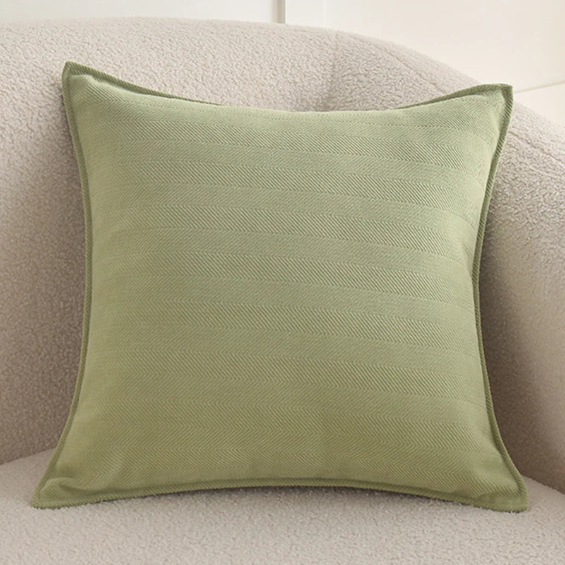 A square, olive green chenille throw pillow cover resting on a light beige sofa.