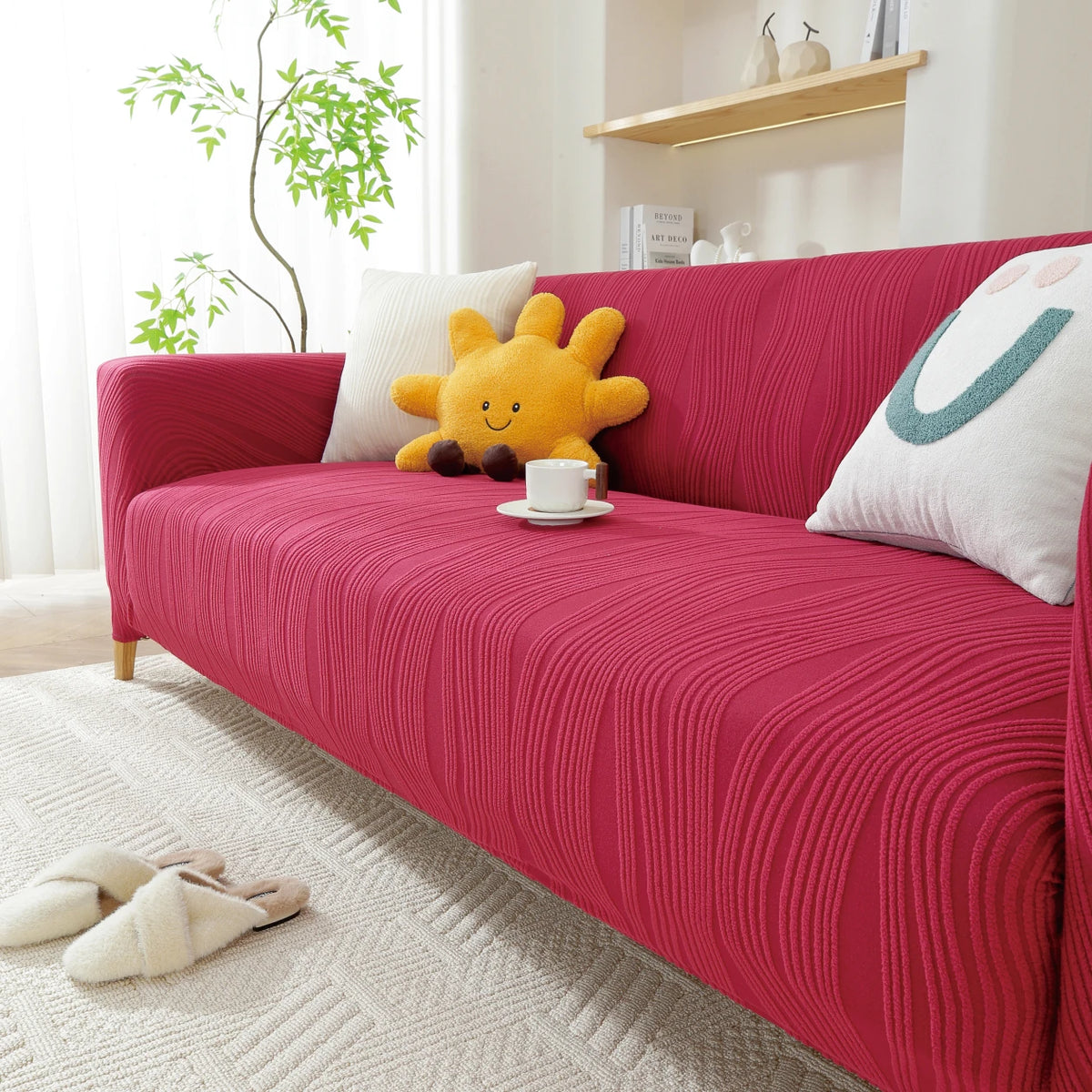 A vibrant pink stretchable sofa cover with a vertical line pattern featuring a yellow stuffed animal and white pillows.
