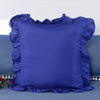 A deep blue ruffled pillow cover displayed on a teal sofa.