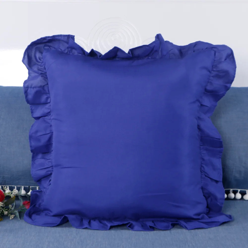 A deep blue ruffled pillow cover displayed on a teal sofa.