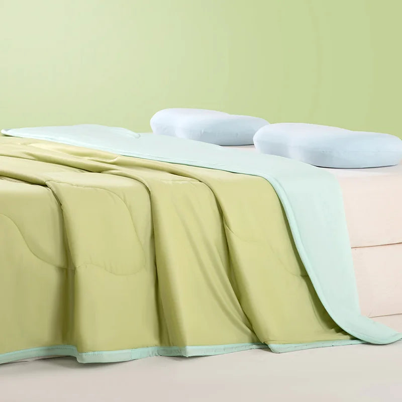 A light green ice silk summer cooling blanket is draped over a pink surface with white pillows.