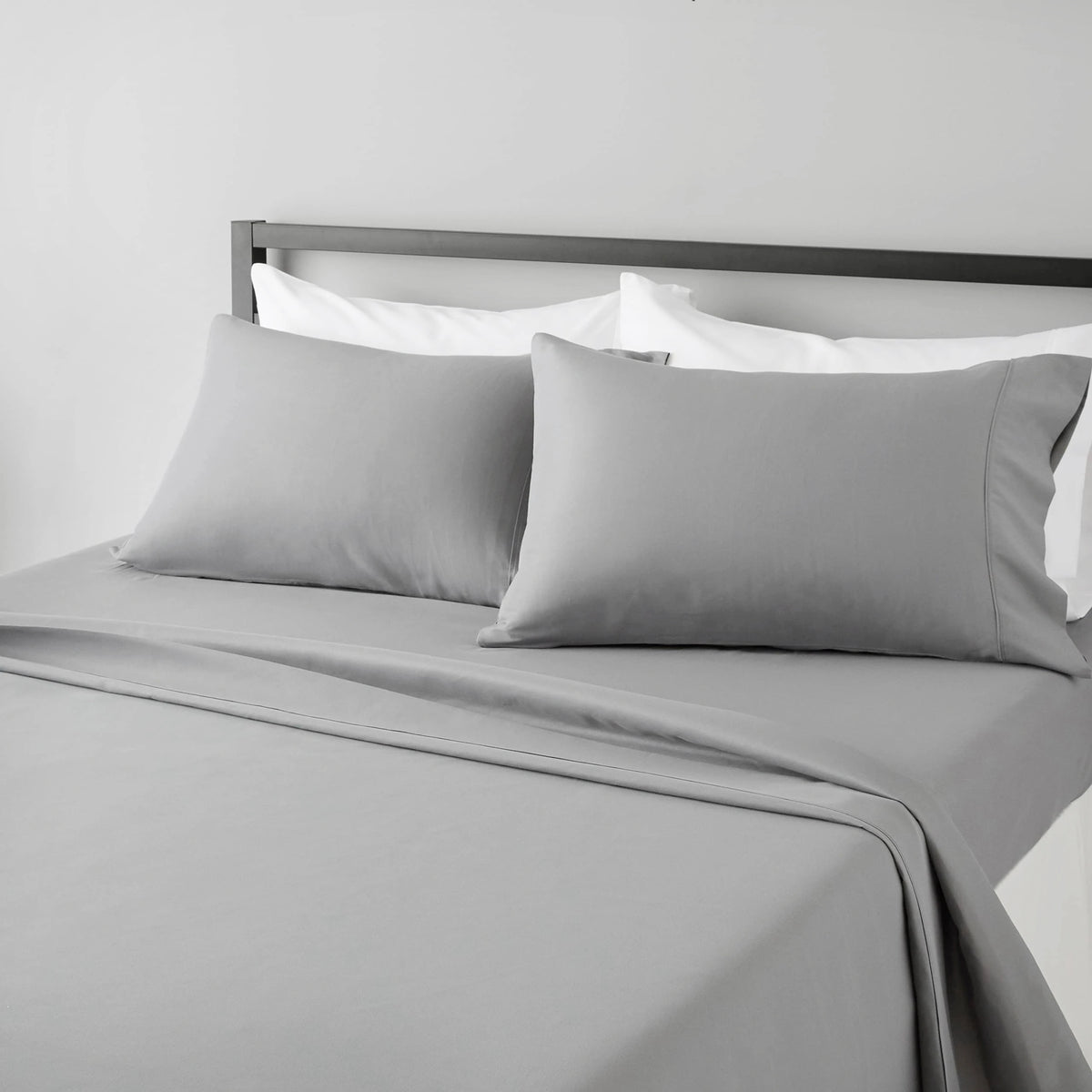 A gray fitted sheet set with white pillowcases is displayed on a bed with a dark headboard.