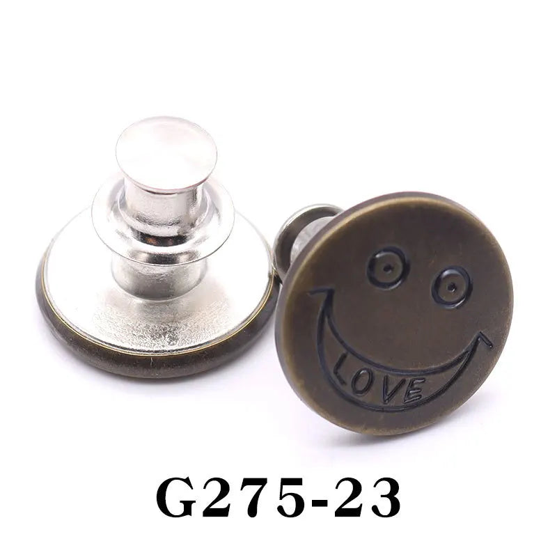 A round, brass-colored button pin with a smiling face engraved on it.