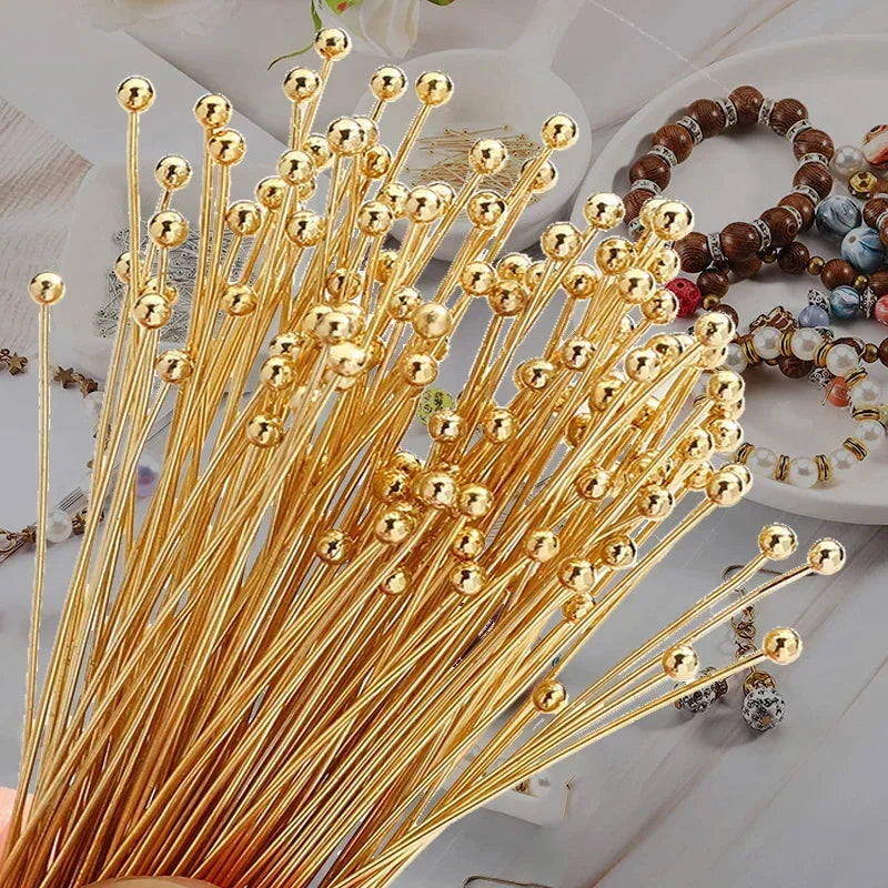 A bundle of gold-colored stainless steel ball head pins for jewelry making arranged on a white surface.