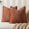A close-up of a textured, rust-colored chenille throw pillow resting on a light-colored surface.