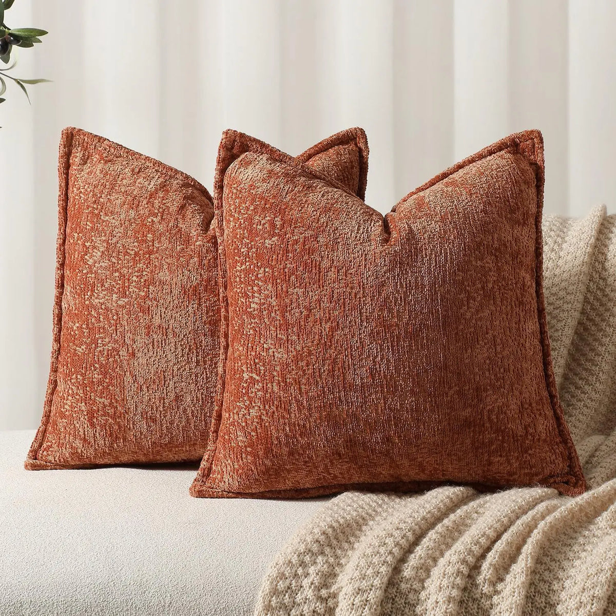 A close-up of a textured, rust-colored chenille throw pillow resting on a light-colored surface.