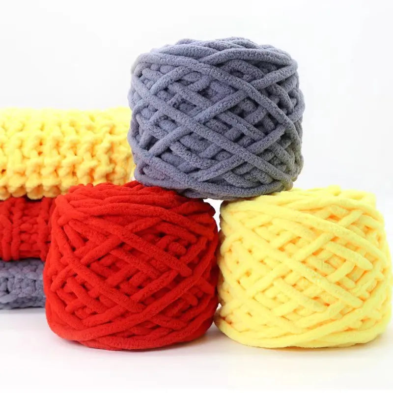 Three skeins of chunky velvet knitting yarn in gray, yellow, and red stacked on a white surface.