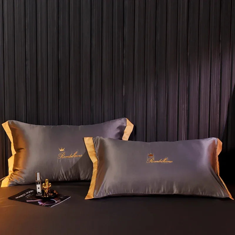 A set of two gray ice silk pillows with gold embroidery against a dark background.