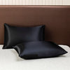A set of black satin flat pillows resting on a beige bed with a brown upholstered headboard.