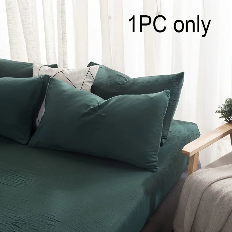 A dark teal pillowcase is shown on a bed with white sheer curtains in a bright room.