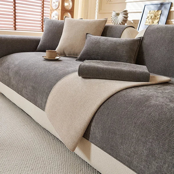 A close-up of a gray chenille sofa cushion cover with beige accent pillows and a light beige throw on a cream carpet.
