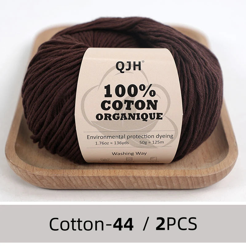 A ball of dark brown organic cotton yarn labeled QJH 100% COTON ORGANIQUE resting on a wooden tray.