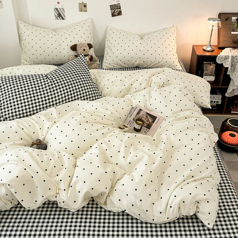 A white duvet cover set with black polka dots and a black and white plaid sheet on a bed.