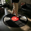 A round black rug with white sound wave patterns and a red center placed on a dark floor.