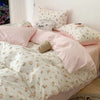 A pink floral bedding set featuring a duvet and pillows with white background and small pink flowers.