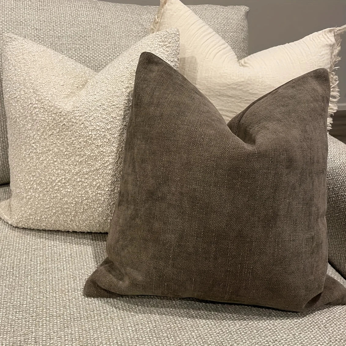 A dark brown linen textured throw pillow resting on a light gray sofa with cream-colored pillows.
