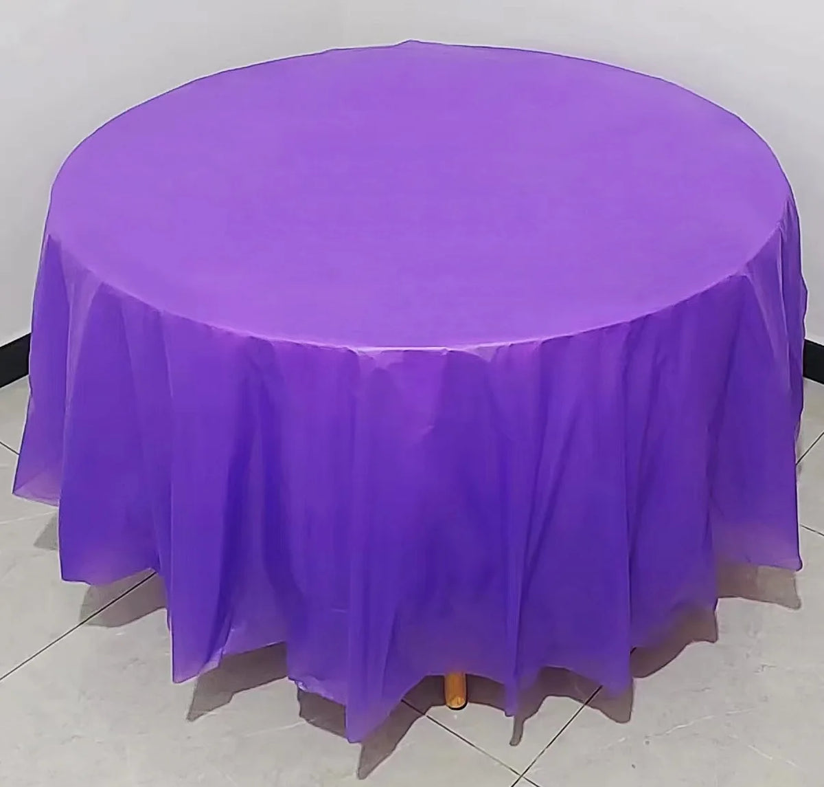 A round purple plastic disposable table cover spread on a white floor.