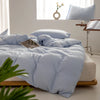 A light blue minimalist duvet cover is spread on a bed with white linens and natural wood accents.