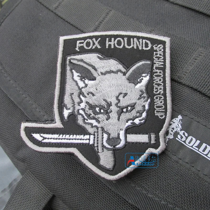A gray uniform patch featuring a stylized foxhound wolf head design and the text FOX HOUND.