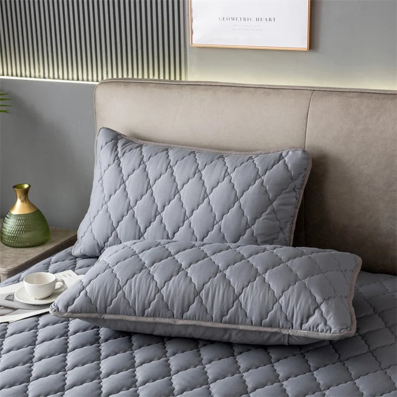 A gray quilted pillow cover resting on a bed, next to a headboard and a small green vase.