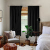 A dark gray waterproof thermal blackout curtain panel hangs in a window next to a bed.