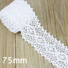A roll of white cotton embroidered lace trim with a delicate openwork pattern shown on a wooden surface.