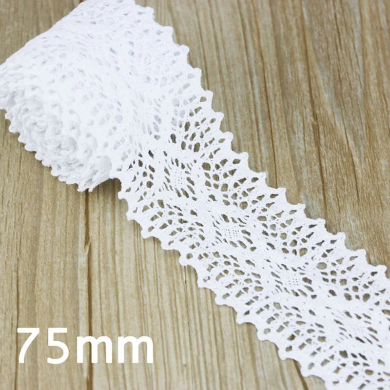 A roll of white cotton embroidered lace trim with a delicate openwork pattern shown on a wooden surface.