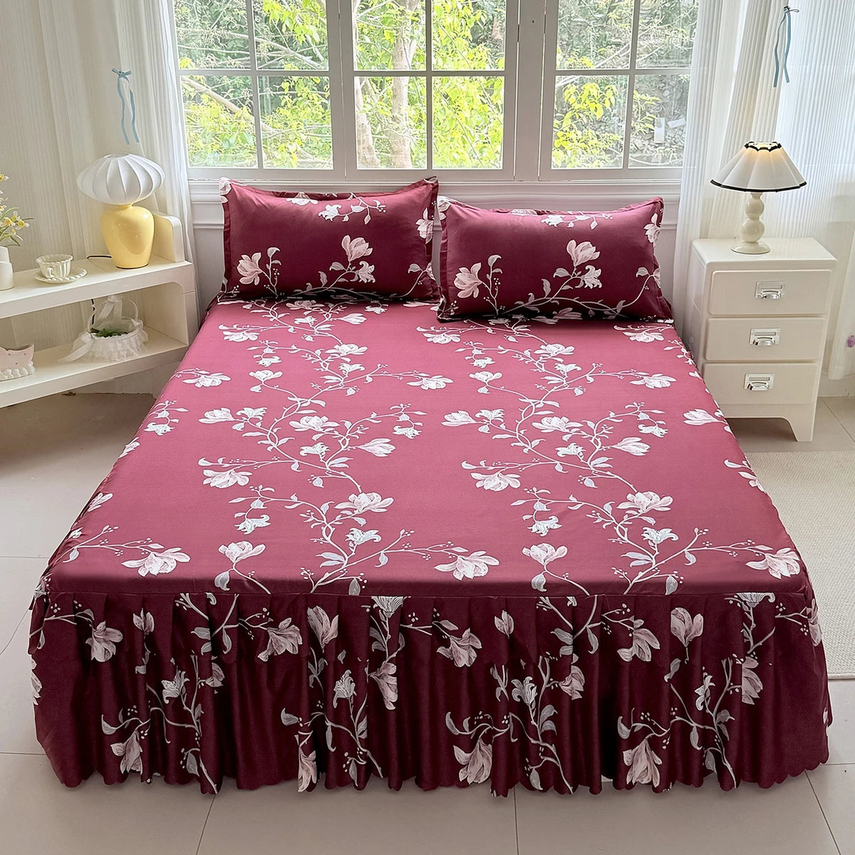A deep magenta bed skirt set featuring a white flower print and matching pillows, displayed in a bright room.