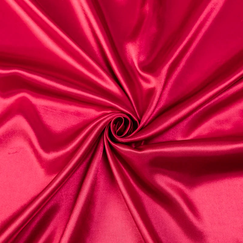 A vibrant magenta satin bedding set with fitted sheets, tightly rolled to show the fabric's sheen.