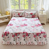 A white bed skirt set with a pink and green floral print displayed on a bed.