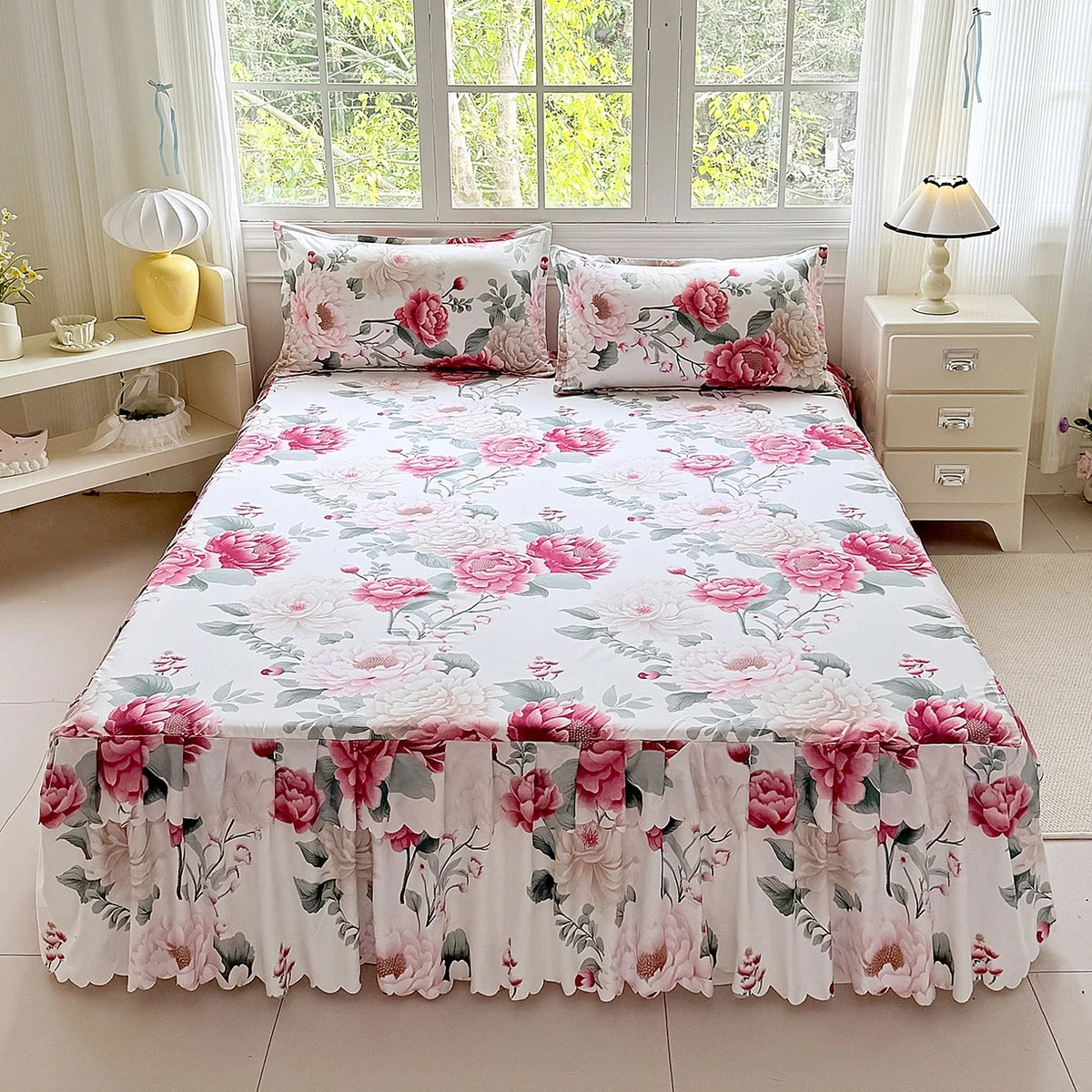 A white bed skirt set with a pink and green floral print displayed on a bed.