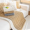 A thick beige flannel sofa pad cover with textured stitching and stacked white and gray cushions.
